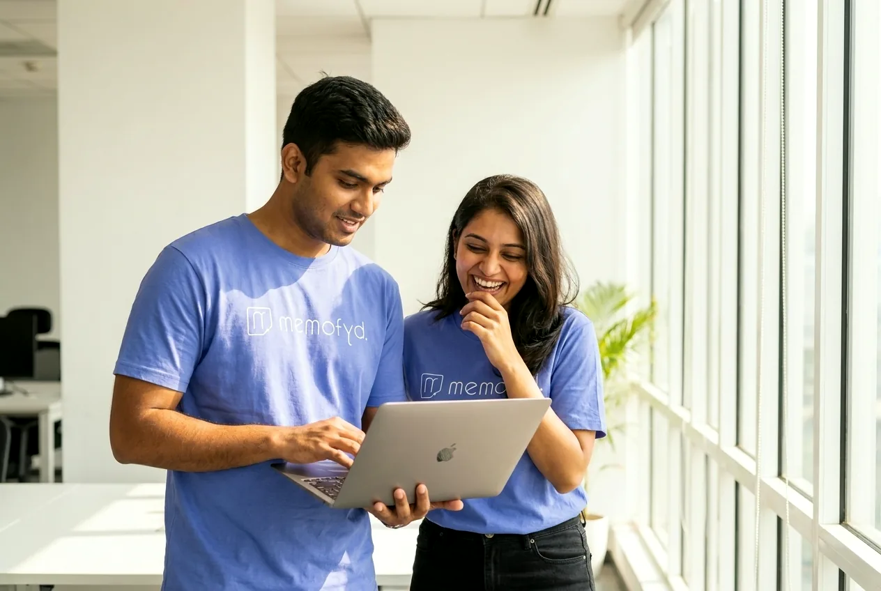 Two colleagues in Memofyd t-shirts looking at a laptop together, one pointing at the screen.