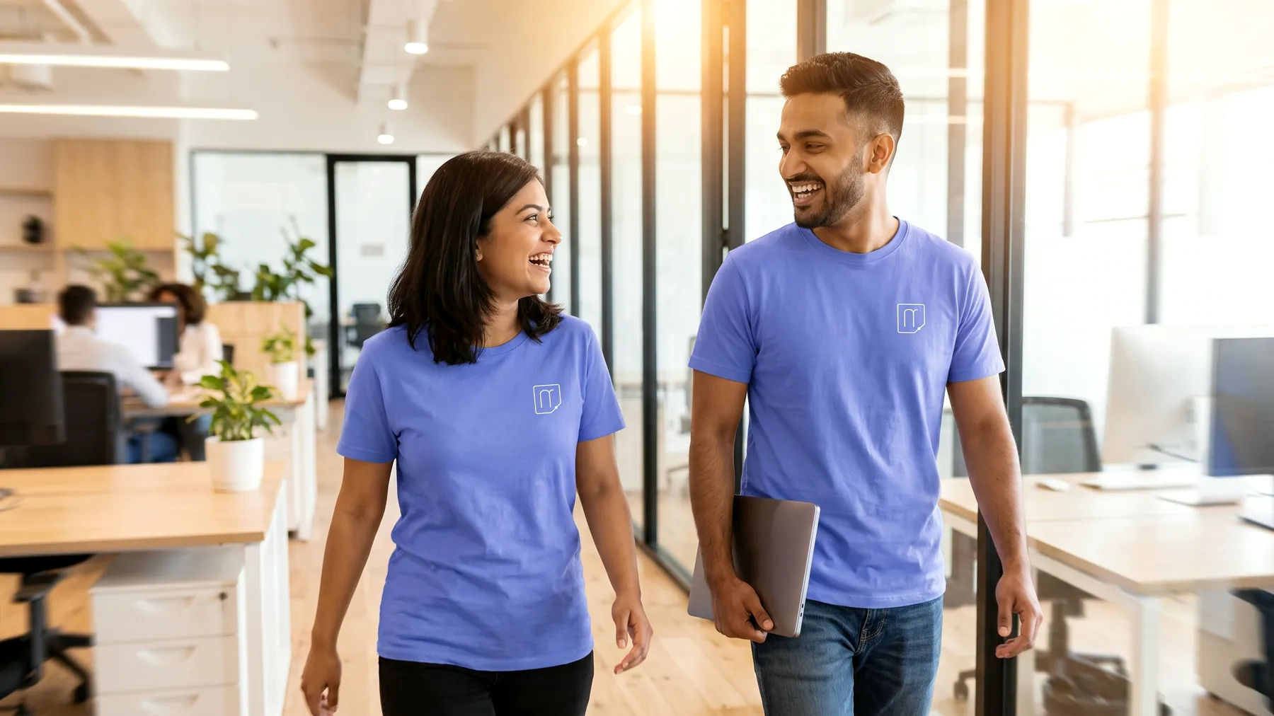 Two colleagues in Memofyd t-shirts walking through a bright open-plan office, laughing.